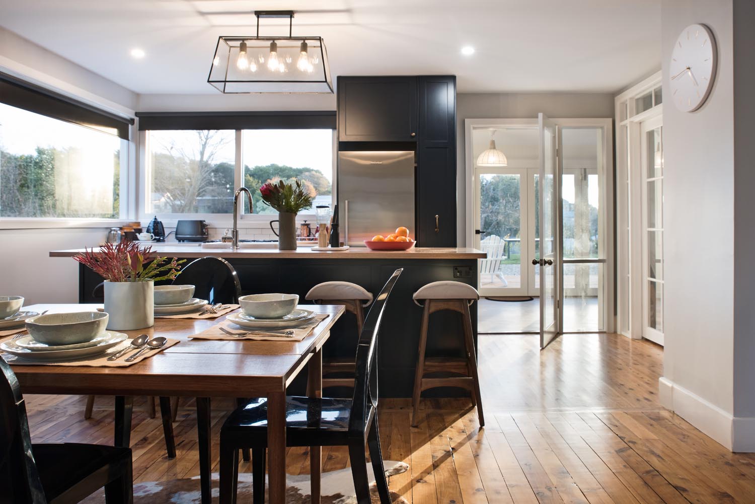 A dark modern kitchen with large windows bordering a styled dinning space